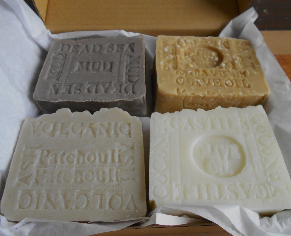 Four different types of soap bars with embossed text on a white surface.