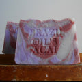 A handmade bar of soap with a marbled purple and pink  acai berry  color , embossed with the text 'BRAZIL OILS ACAI'.
