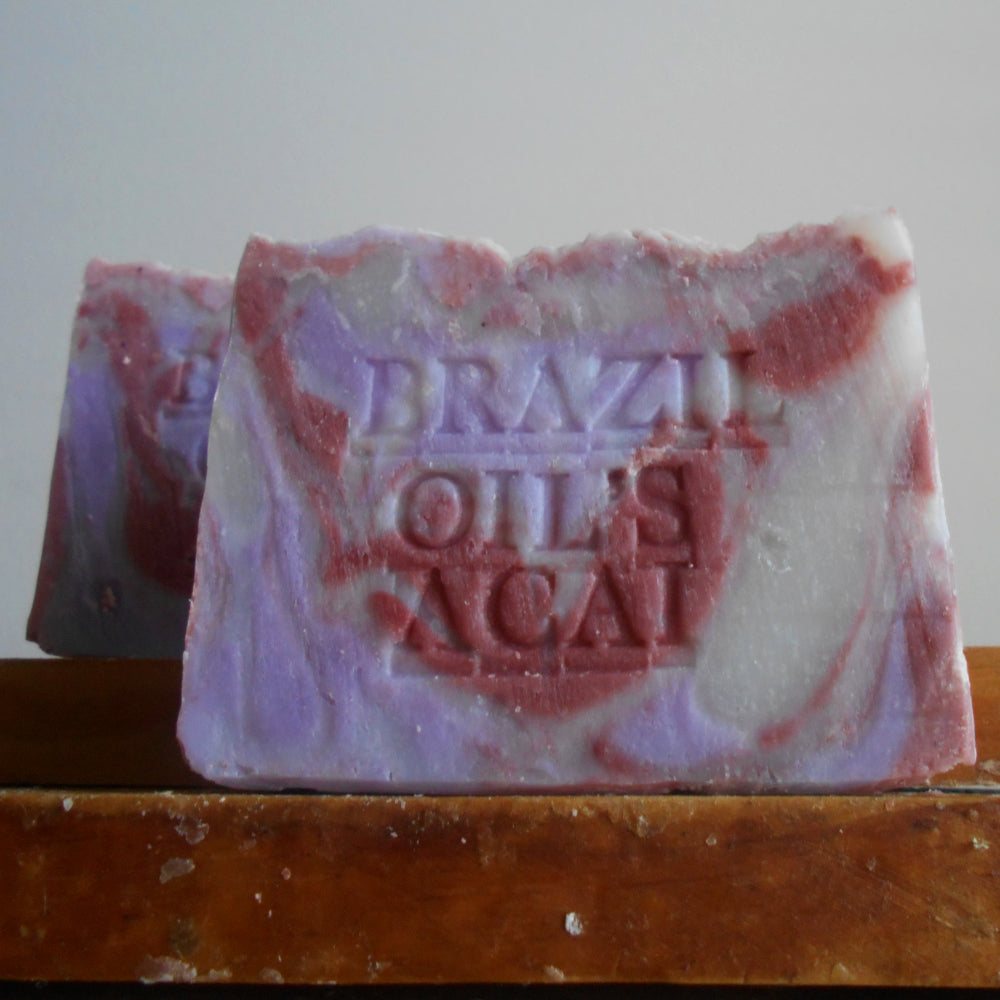 A handmade bar of soap with a marbled purple and pink  acai berry  color , embossed with the text 'BRAZIL OILS ACAI'.