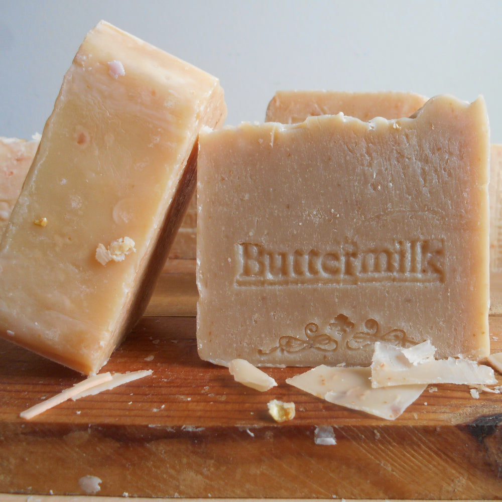 Buttermilk soap handmade buttermilk soap on a wooden board, one standing upright and one lying down showing the embossed brand name 'Buttermilk'.