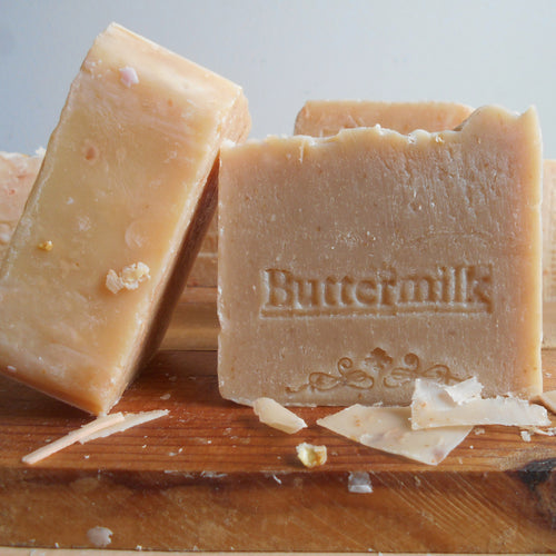 Buttermilk soap handmade buttermilk soap on a wooden board, one standing upright and one lying down showing the embossed brand name 'Buttermilk'.