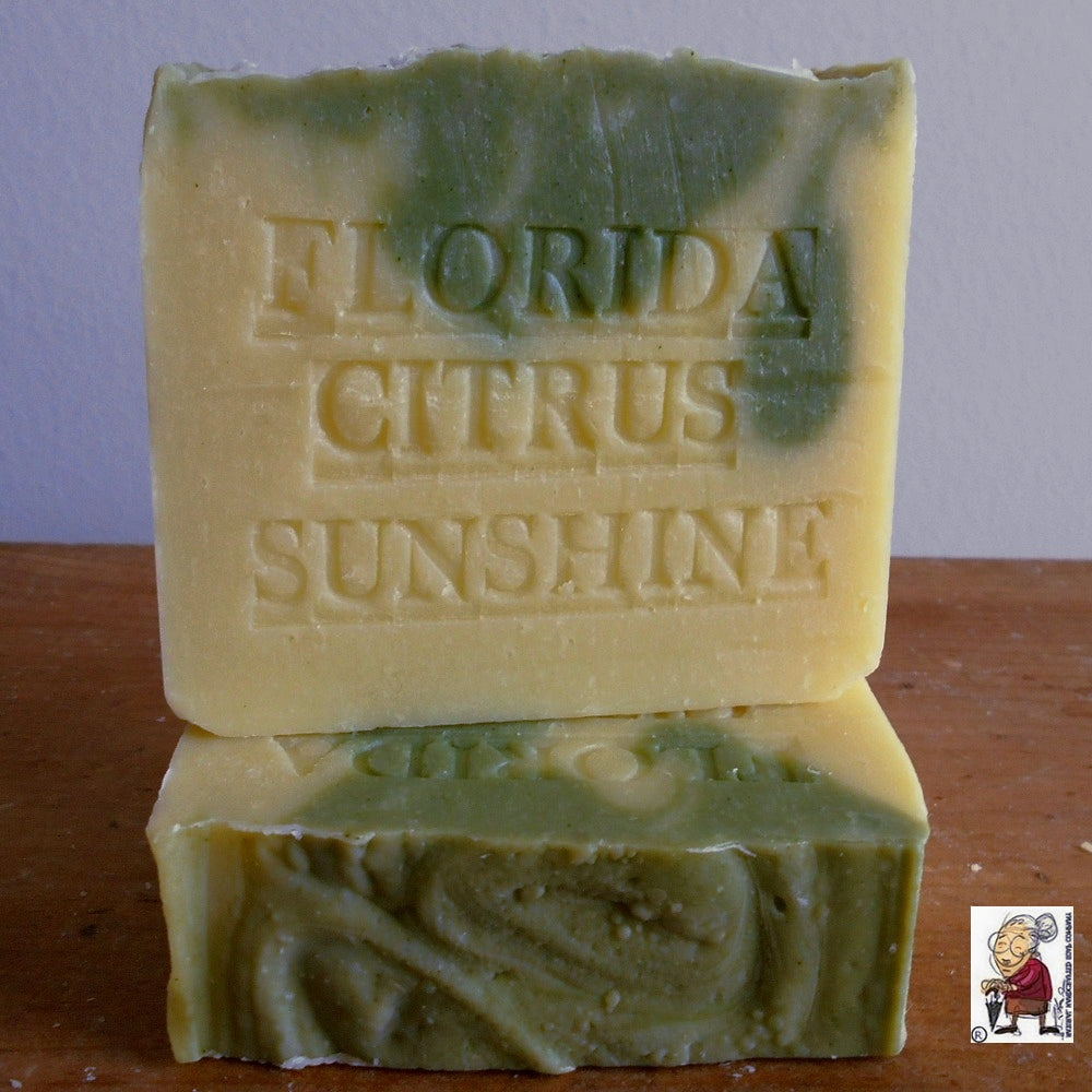 A Natural Citrus Handmade Soap Tangerine bar . The top layer is green with uneven, wavy textures, while the bottom layer is yellow. The Natural Citrus Handmade Soap Tangerine has the words "FLORIDA CITRUS SUNSHINE" embossed on it. There is a small logo in the bottom right corner from Natural Handcrafted Soap.