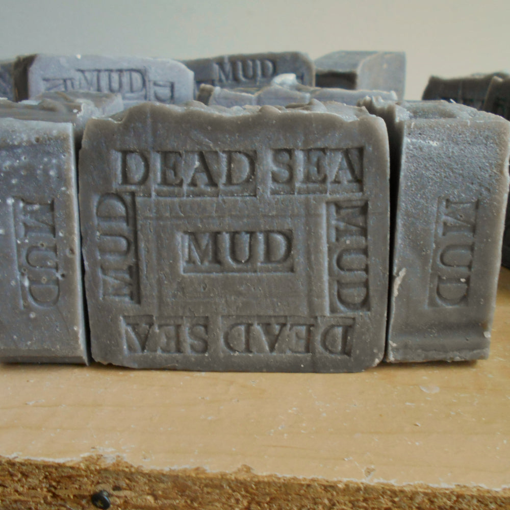 Soap made with Dead Sea Mud Print  'DEAD SEA MUD' and 'MUD' stacked on a tan surface against a light neutral background.