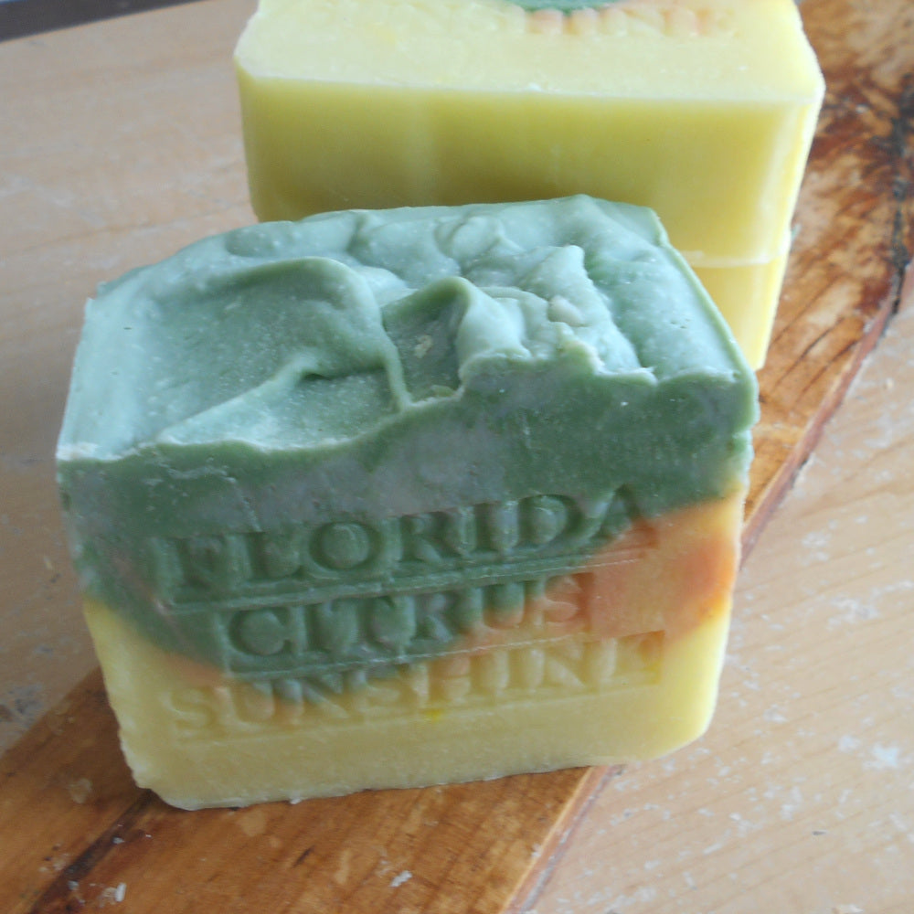 Two bars of soap, one green and one yellow, on a wooden surface with 'Florida Citrus Sunshine  Stamp and branding colors 
