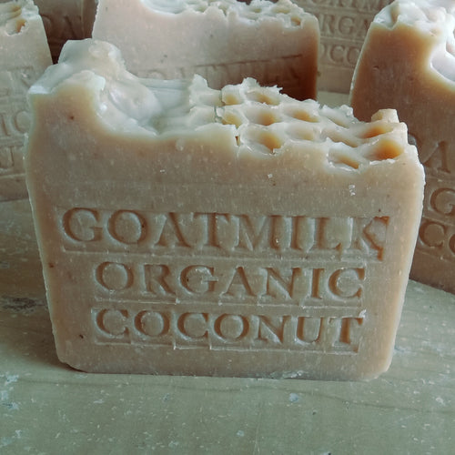 Close-up of handcrafted moisturizing soap bars with "Goat Milk and Organic Coconut Milk Soap" embossed on the front. The soap has a rustic appearance, with a natural beige color and a slightly rough texture, giving it an artisanal look. This product is made by Grandmas All Natural Soap.