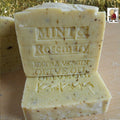 Two bars of soap with 'Mint & Rosemary' and 'Extra Virgin Olive Oil' text on a wooden surface.