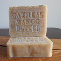 Two bars of oatmeal mango butter soap stacked on a wooden surface with a neutral background. Grandma's Organic  Oatmeal Soap