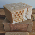 milk soap bar of honeycomb-patterned soap in a warm milk color  tone, shown resting on top of a brown cardboard soap box on a wooden surface.