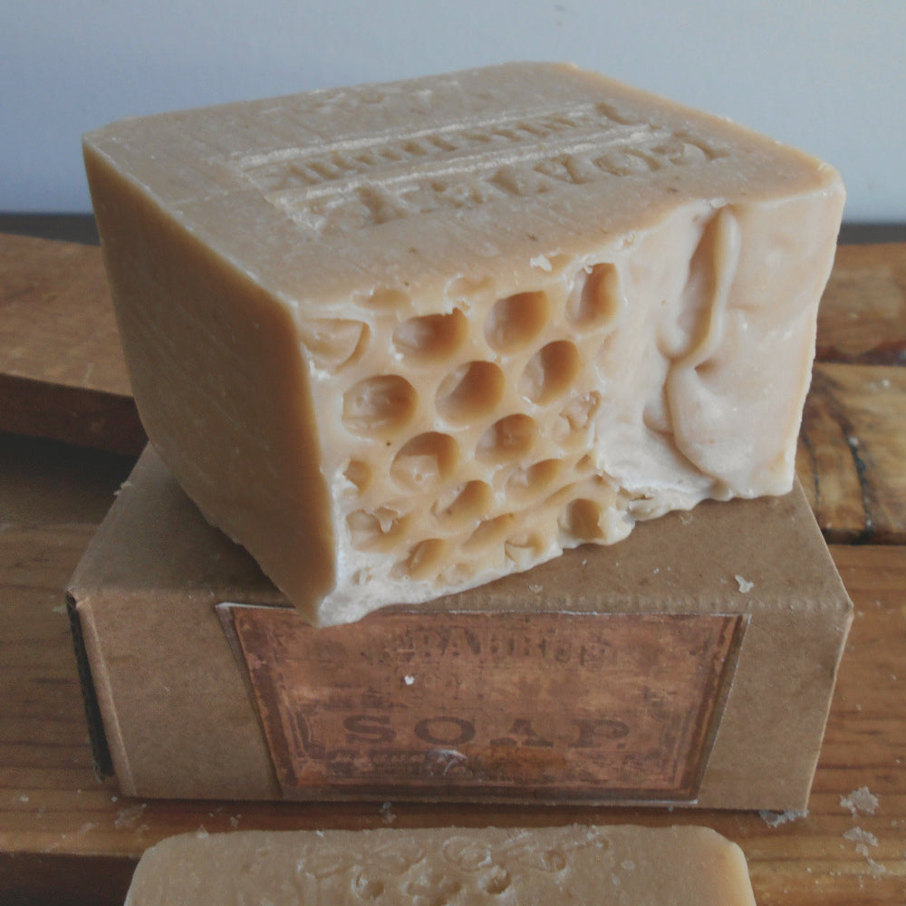 milk soap bar of honeycomb-patterned soap in a warm milk color  tone, shown resting on top of a brown cardboard soap box on a wooden surface.