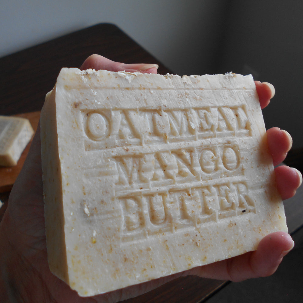 Bar of soap with 'Oatmeal Mango Butter' text held in a hand.