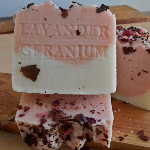 Two bars of lavender geranium soap  and roses petals on a wooden surface