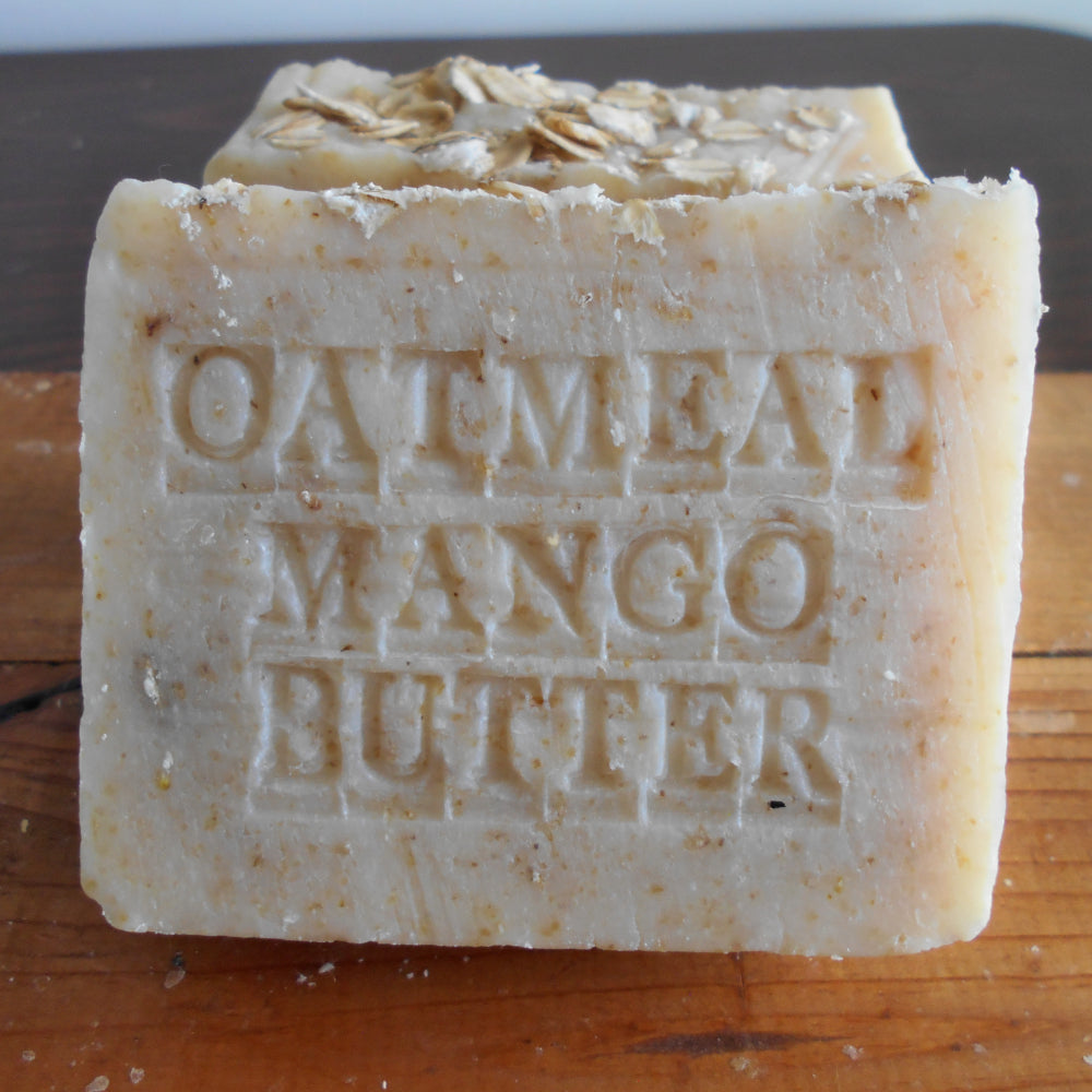 A rectangular bar of Grandmas All Natural Soap’s Organic Oatmeal Soap with Mango Butter Fragrance Free, ideal for sensitive skin, rests atop another bar. "OATMEAL MANGO OATMEAL" is engraved on it,
