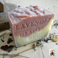 All Natural Soap’s French Provence Lavender with Dead Sea Mud Limited Aged Bar 15 Oz—a handcrafted soap with pink and cream layers, embossed and surrounded by dried flowers on wood.