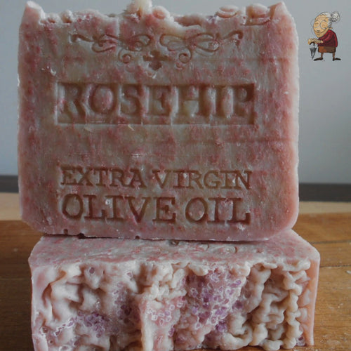Artisan Rosehip Soap with Extra Virgin Organic Olive Oil and Mediterranean Sea Salt .The soap bars have a natural, rustic appearance, with some texture on the surface, and are displayed on a wooden stand.
