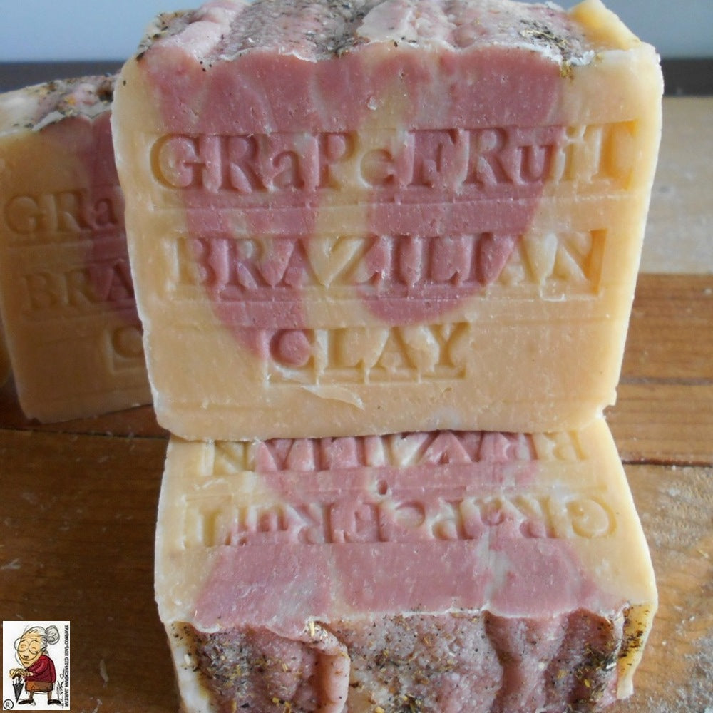 Close-up of two bars of Natural Soap African Grapefruit stacked, with the top one showing "Grapefruit" and "Brazilian Clay" engraved on it. The soap, rich in antioxidants and a source of Vitamin C, appears to be a blend of pink and orange hues. 