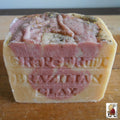 Natural Soap African Grapefruit stacked, with the top one showing "Grapefruit" and "Brazilian Clay" engraved on it. The soap, rich in antioxidants and a source of Vitamin C, appears to be a blend of pink and orange hues.